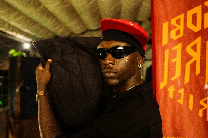 Man in red hat and sunglasses carries large bag